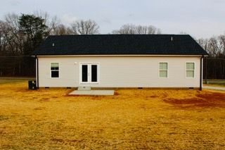 A white house with a black roof is sitting in the middle of a field.