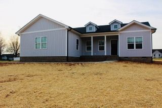 A large white house with a porch is sitting on top of a dry grass field.