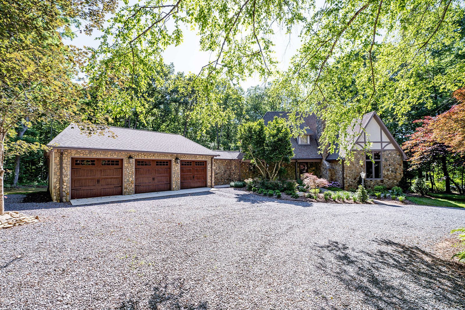 A large house with three garages and a gravel driveway surrounded by trees.