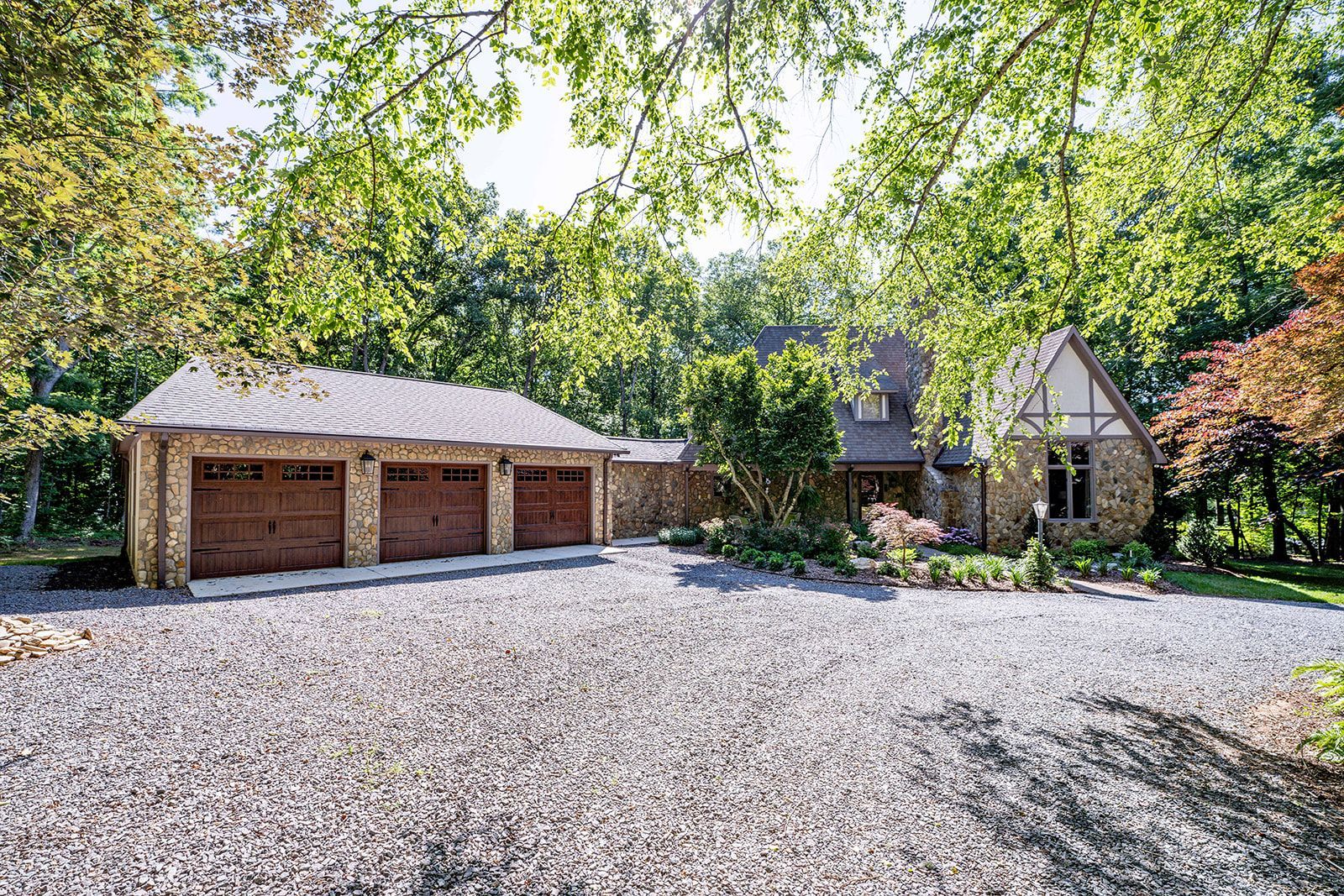 A large house with three garages and a gravel driveway in front of it.