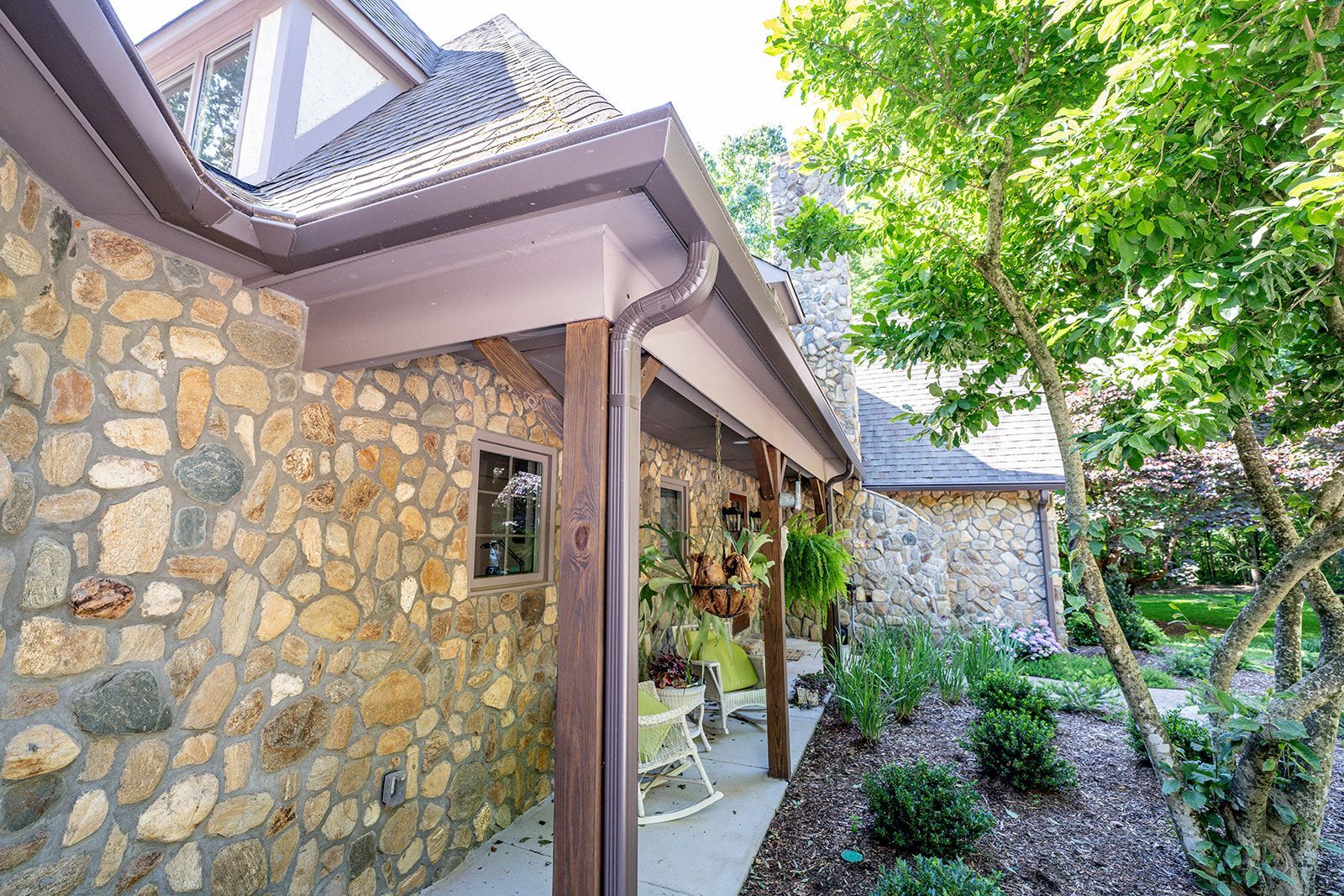 A stone house with a porch and rocking chairs in front of it.