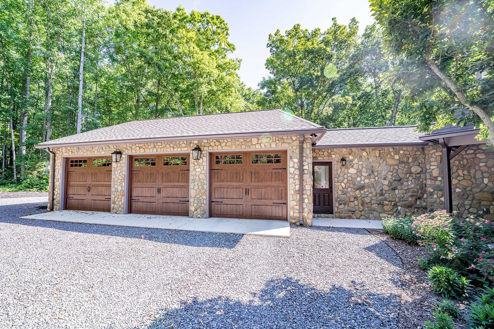 A large stone garage with three garage doors is surrounded by trees.