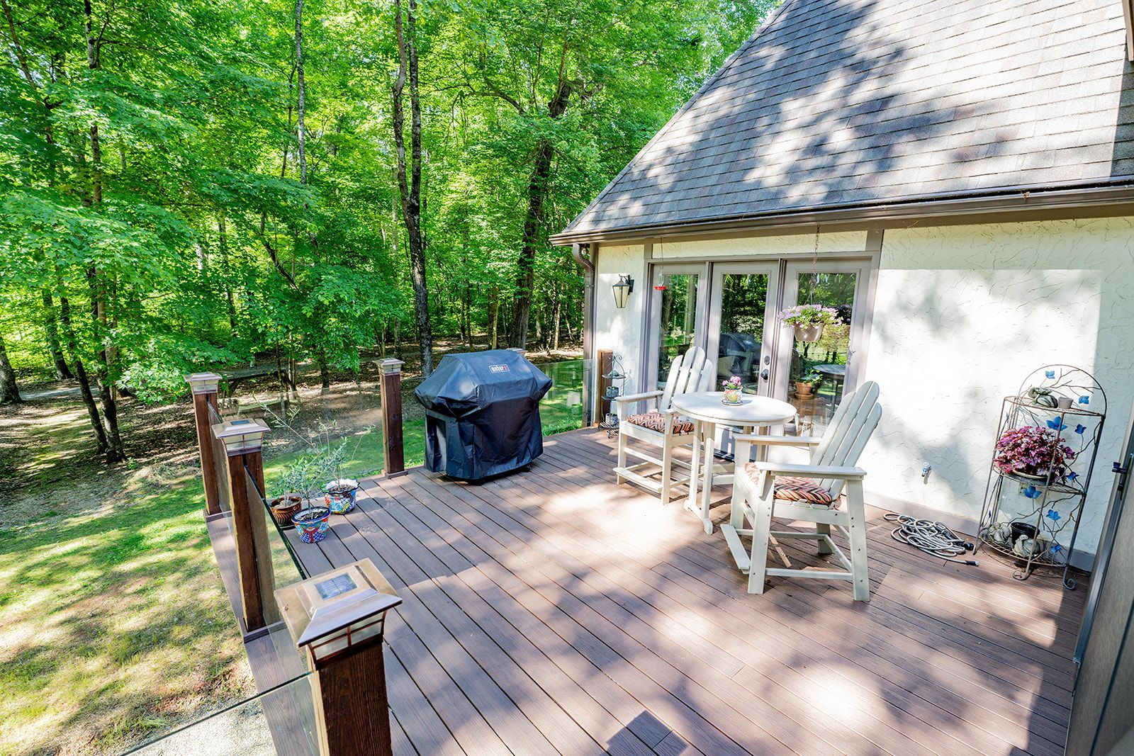 There is a deck with a grill and chairs on it in front of a house.