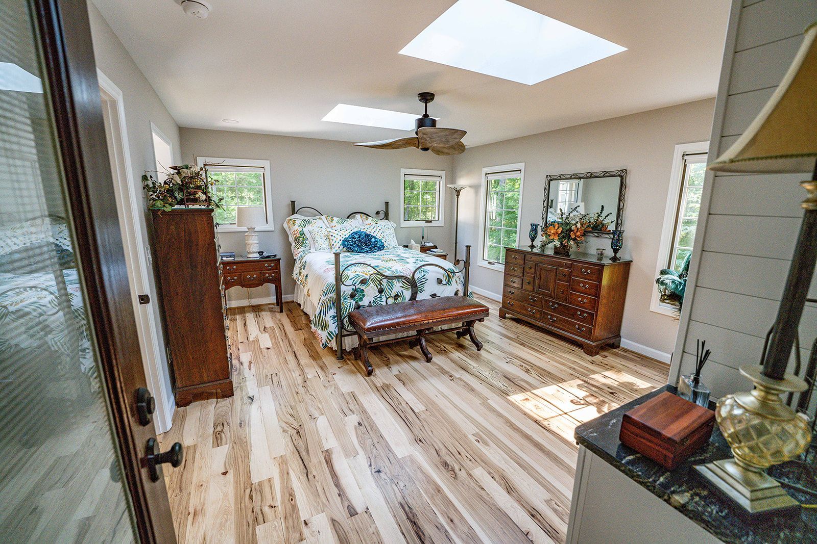 A bedroom with a large bed , dresser , mirror and ceiling fan.