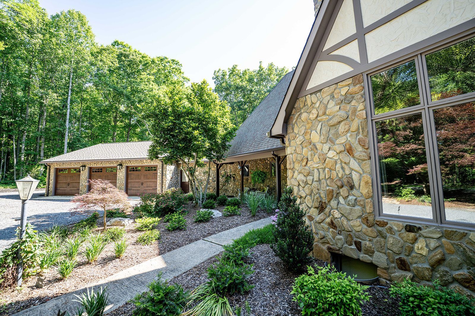A stone house with two garages and a walkway in front of it surrounded by trees.