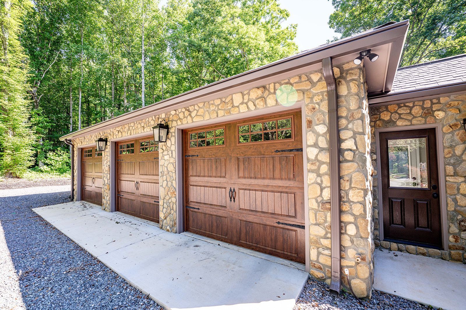 A house with three garage doors and a stone wall.