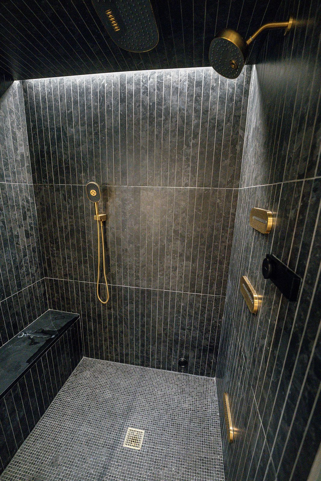 A shower with a black tile floor and a gold shower head.