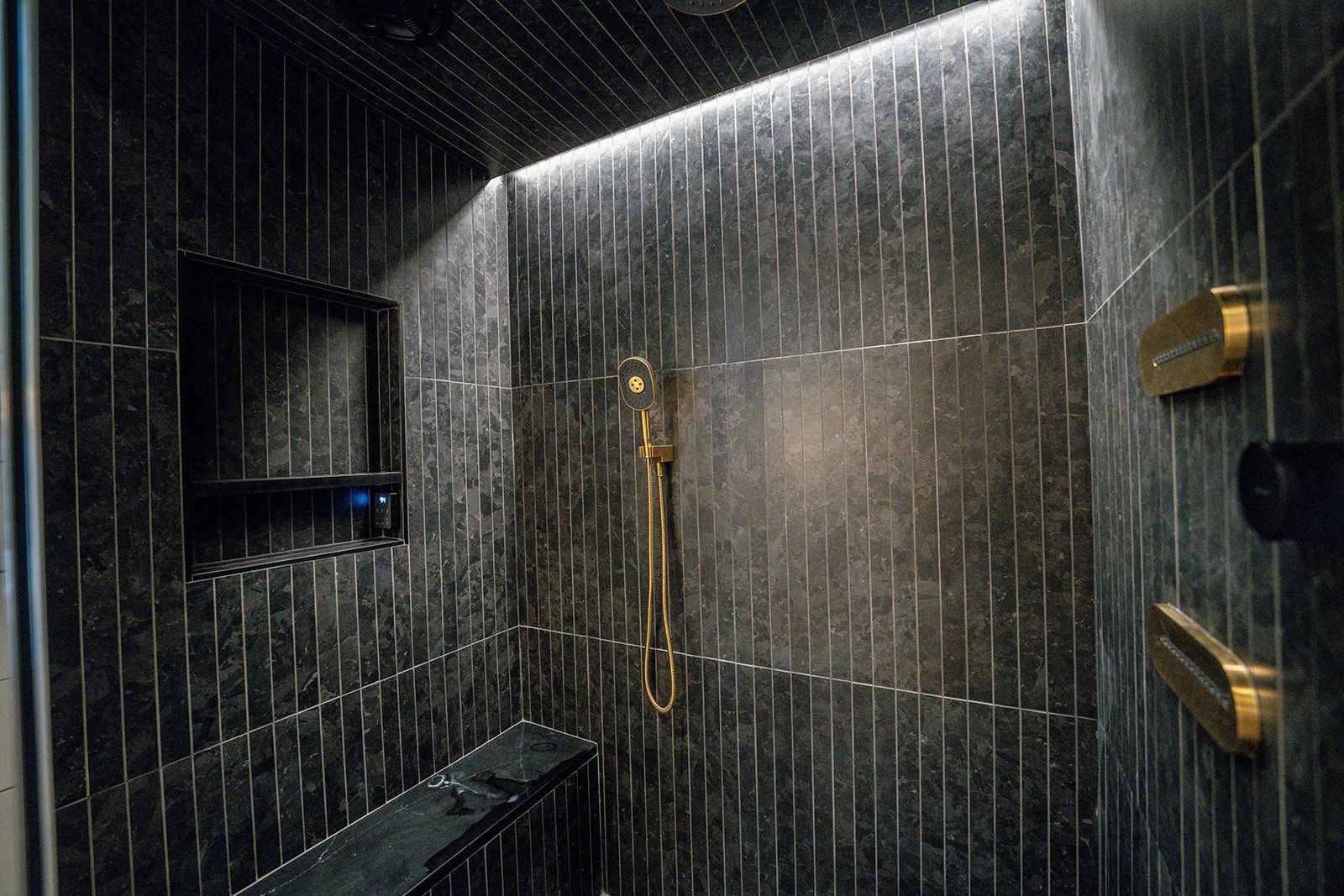 A bathroom with black tiles and a shower head.