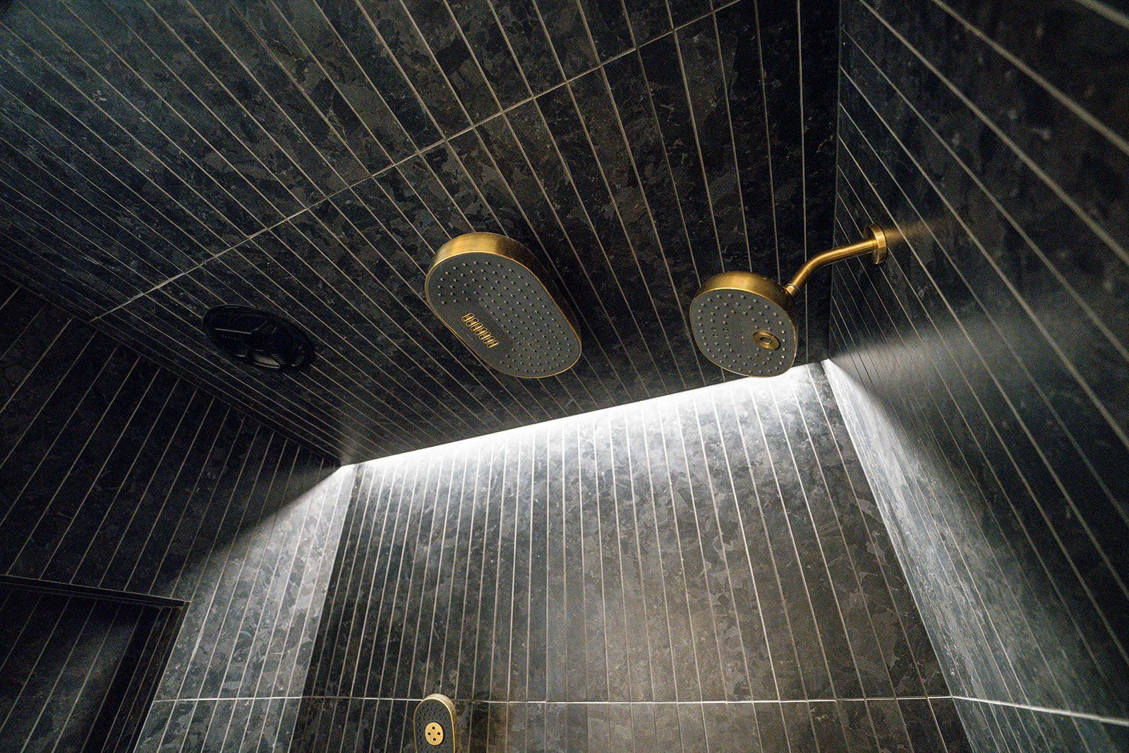 A shower with two shower heads and a light on the ceiling.