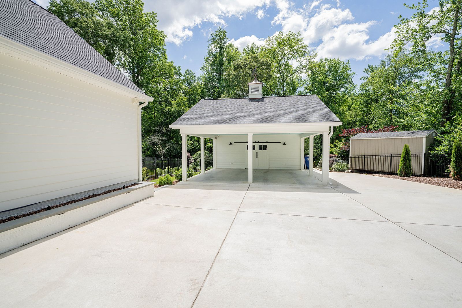 A white garage with a gray roof is sitting next to a white house.