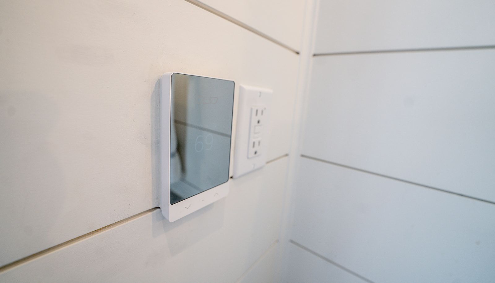 A mirror is hanging on a white wall next to an electrical outlet.