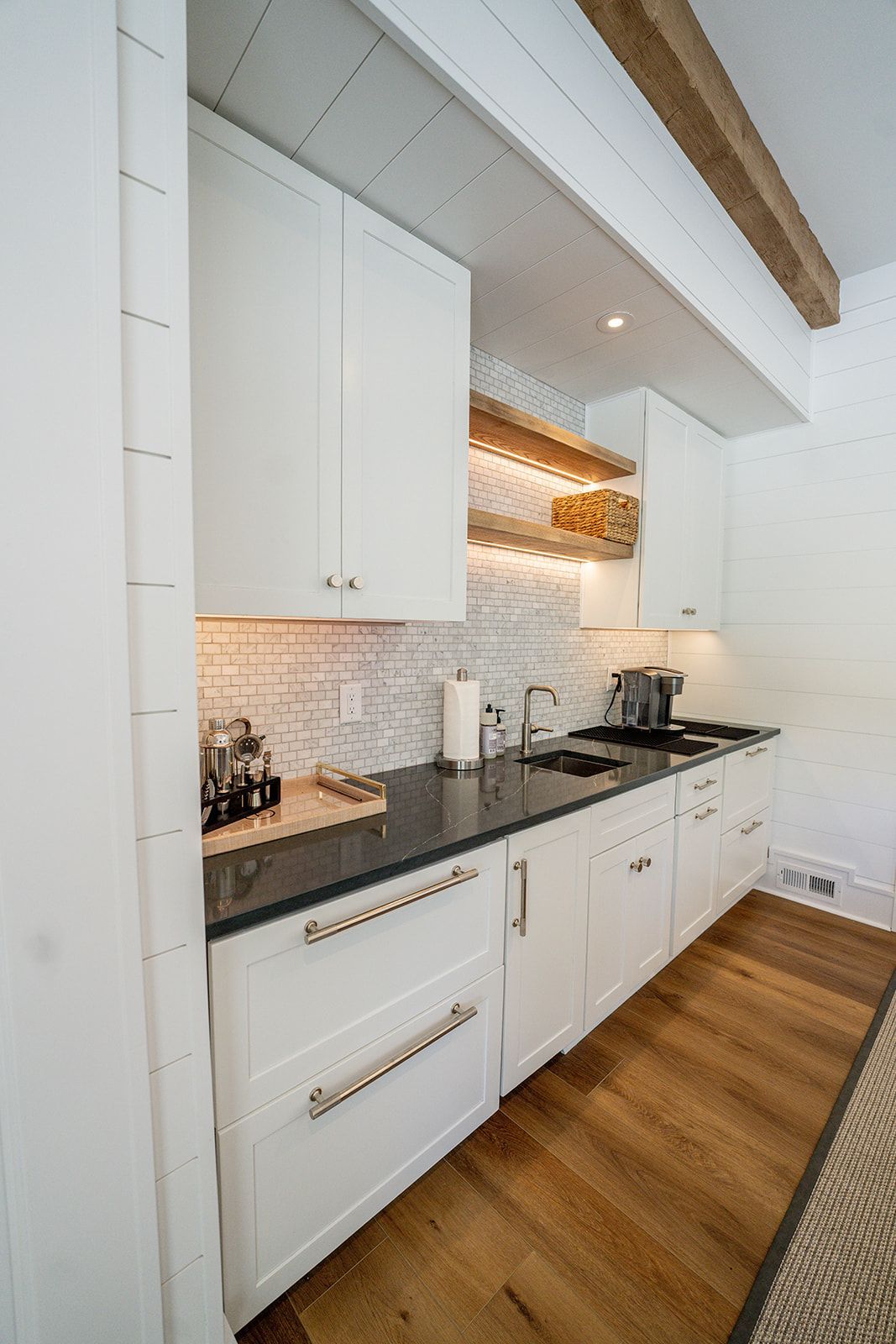 A kitchen with white cabinets , black counter tops , and wooden floors.