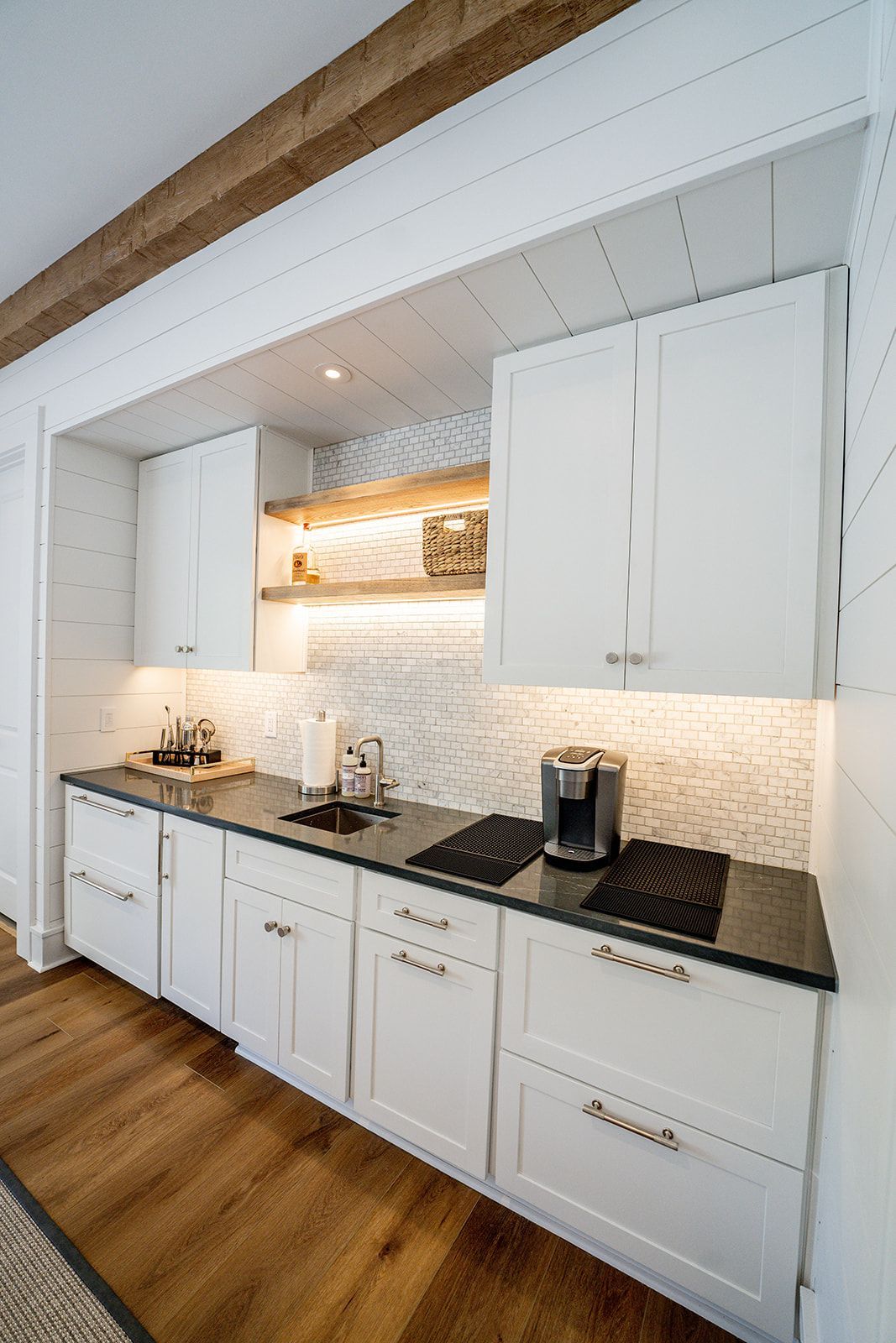 A kitchen with white cabinets , black counter tops , and wooden floors.