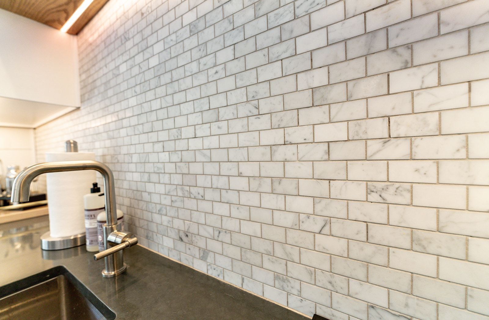 A kitchen with a sink , faucet , and marble tiles on the wall.