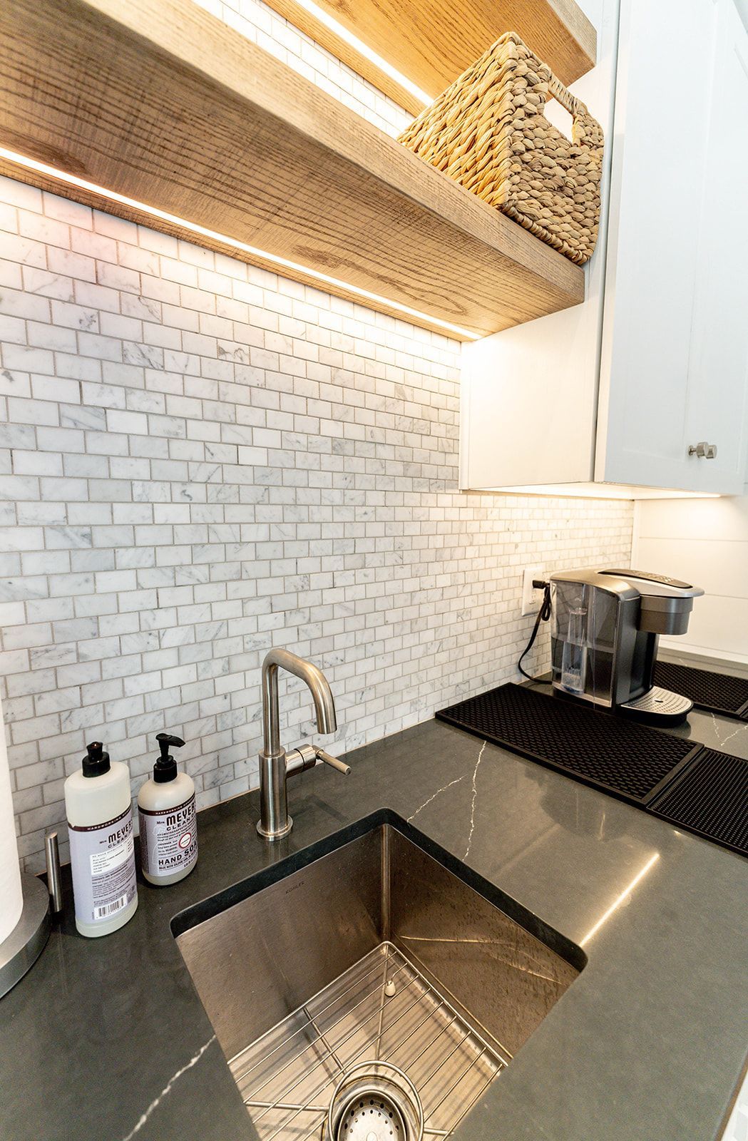 A kitchen with a stainless steel sink , soap dispensers , and a coffee maker.