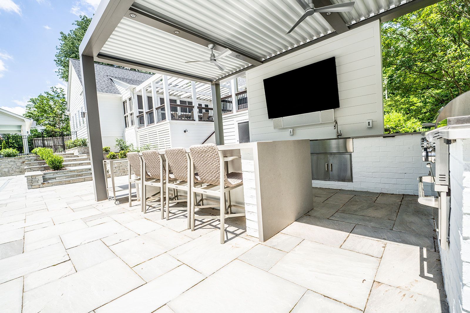 A patio with a grill , stools , a television and a ceiling fan.