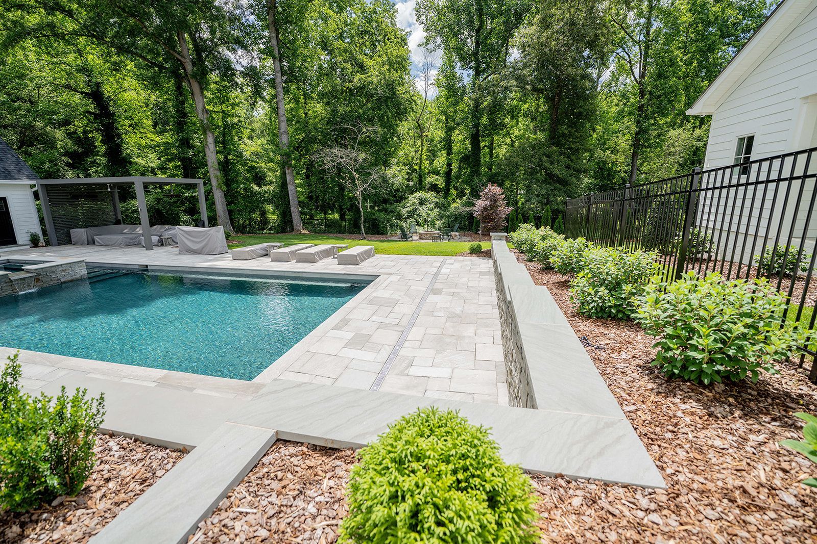 A large swimming pool in the backyard of a house surrounded by trees.