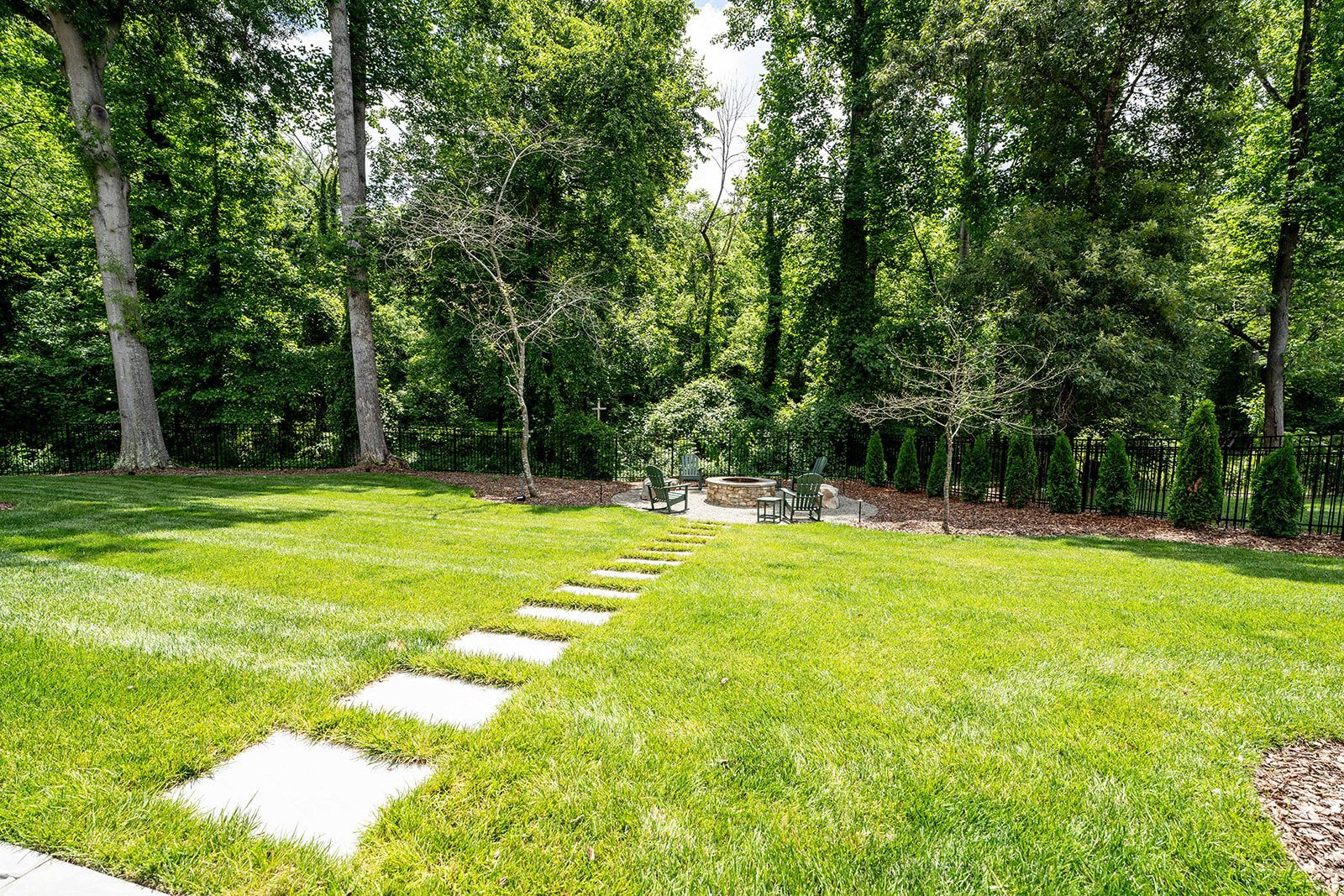 A lush green lawn with a stone walkway leading to a forest.