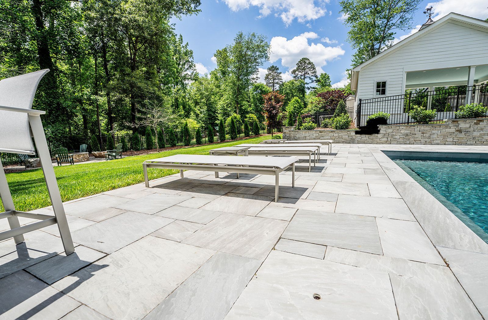 A patio with chairs and a swimming pool in the backyard of a house.