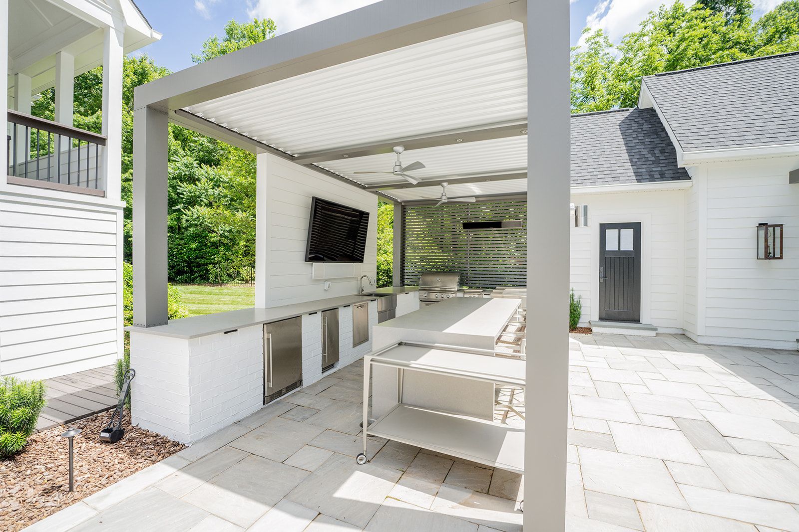 A white house with a patio area and a pergola in front of it.