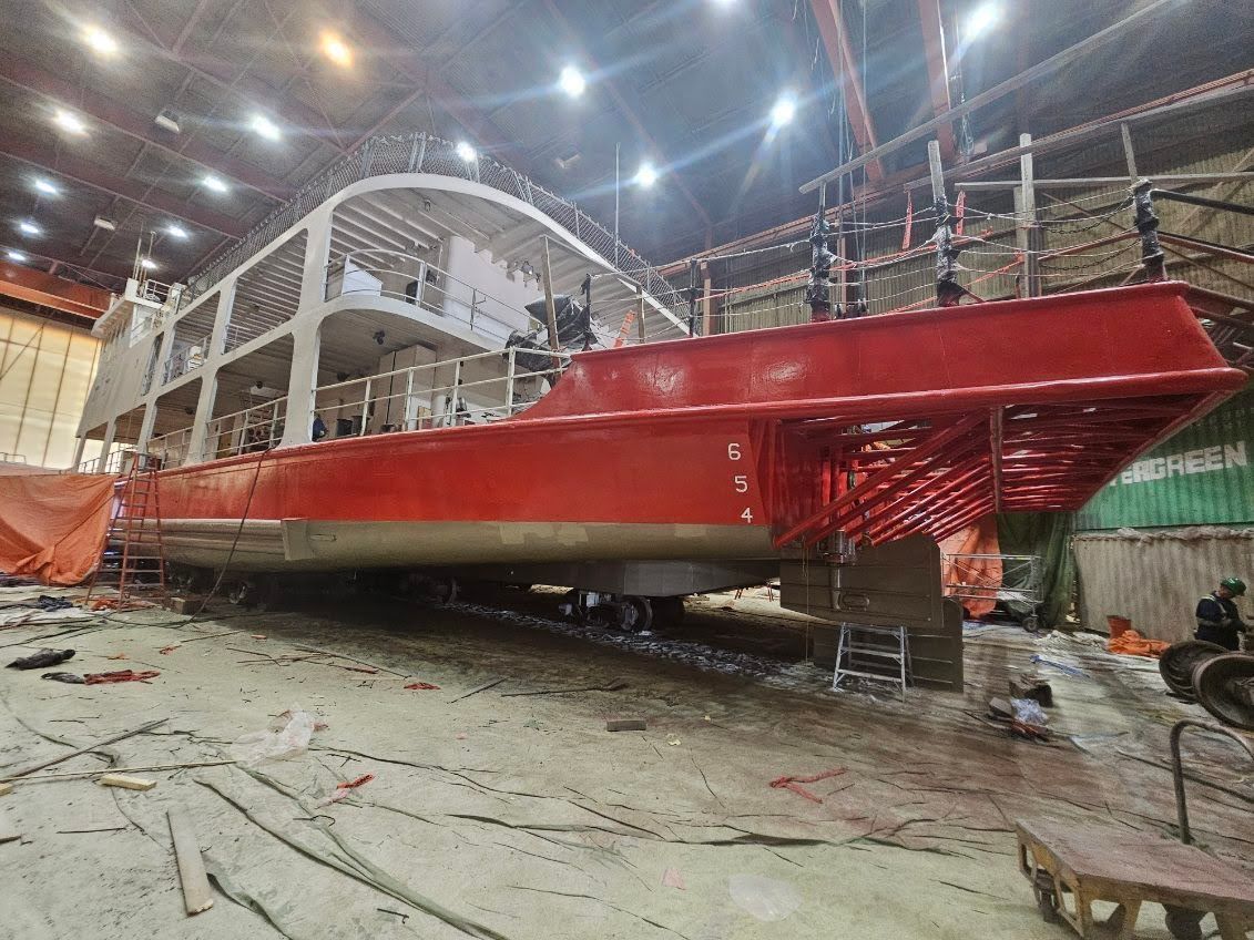 Marine vessel receiving a fresh red protective coating inside an industrial facility