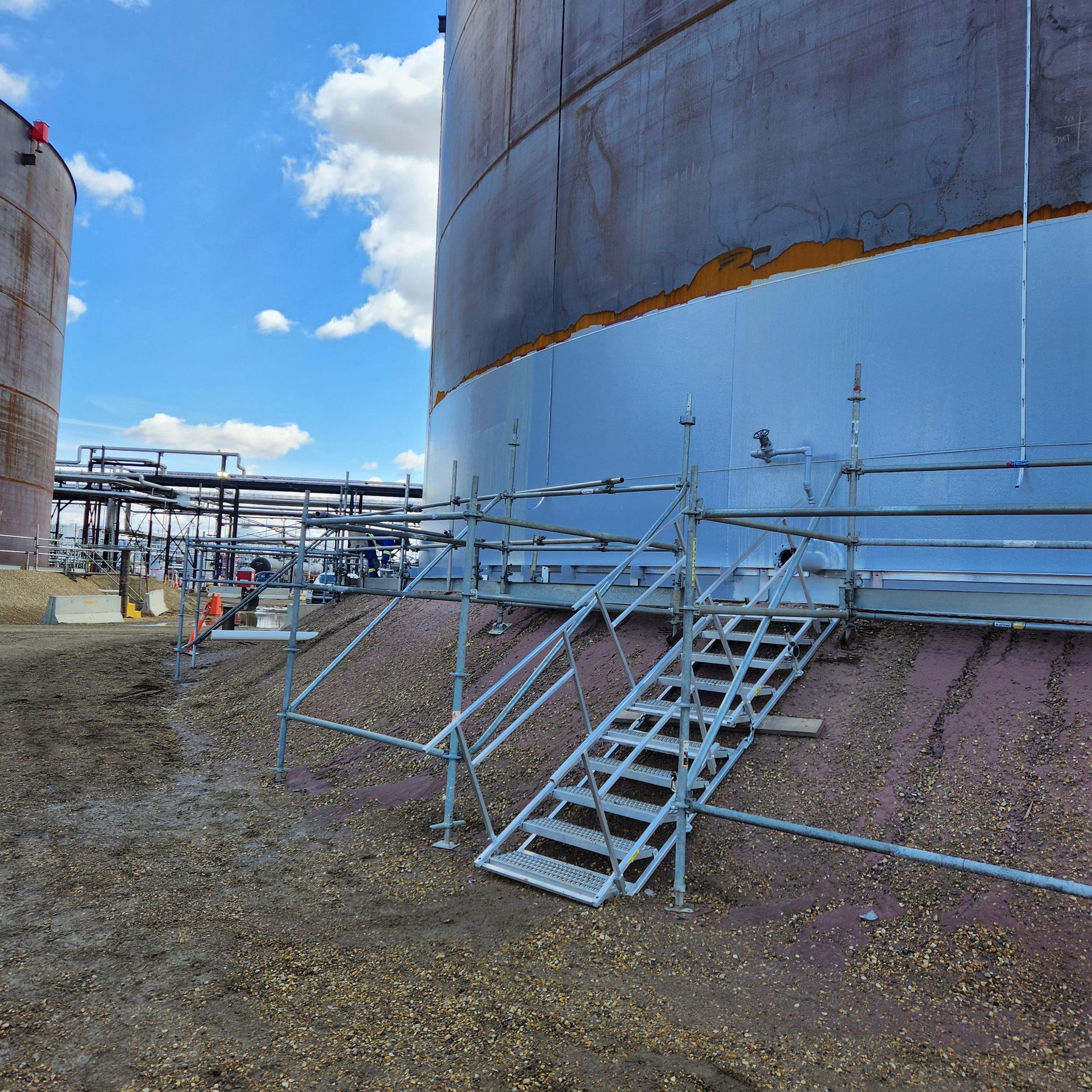 Storage tank mid-process during exterior tank painting, with visible contrast between coated and uncoated surfaces
