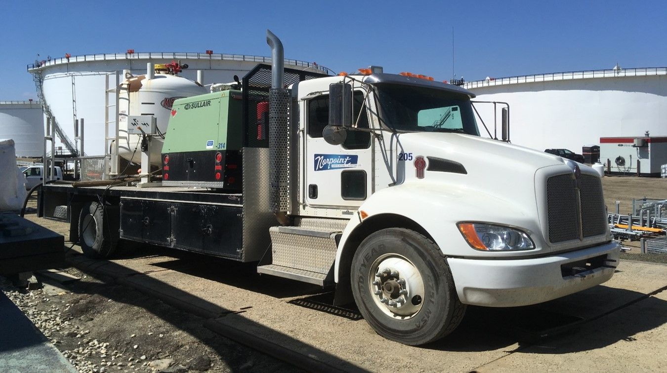 Norpoint truck equipped with coating application machinery parked near industrial tanks