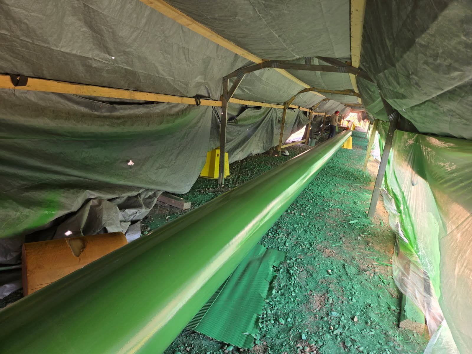 Pipeline construction site with green-coated pipe under temporary protective tent structure
