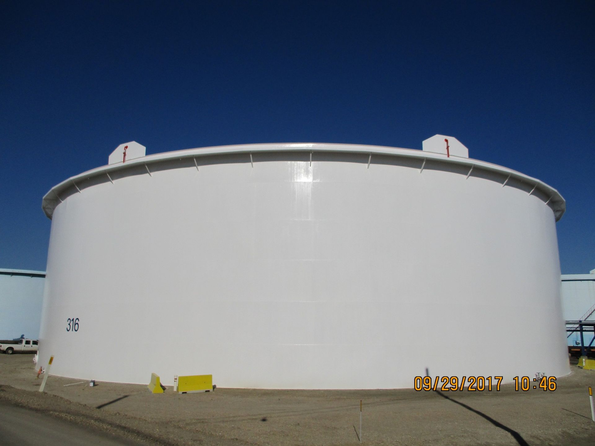 Large industrial tank with a freshly applied white protective coating under a clear blue sky