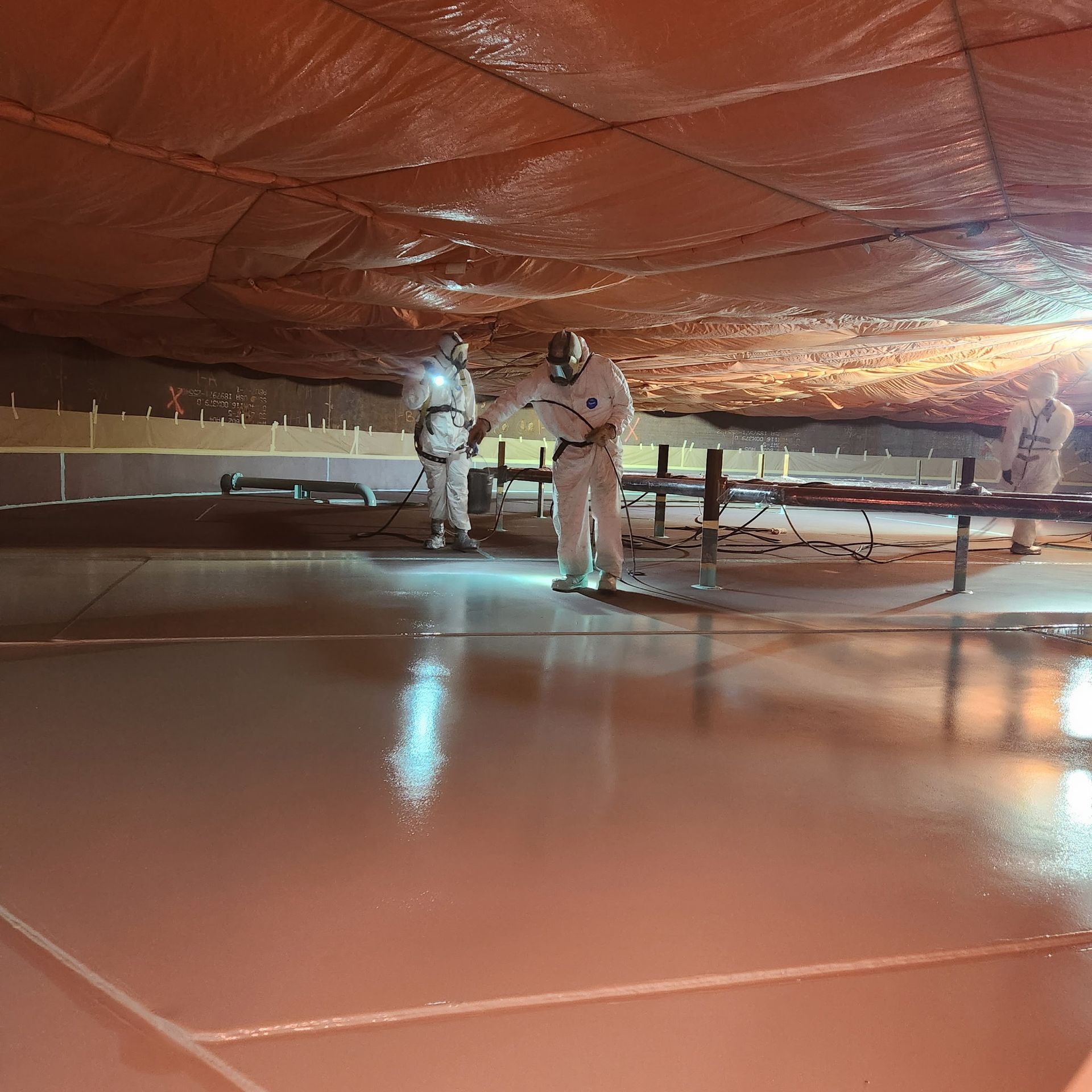 Crew in protective gear performing interior tank painting, applying high-performance coatings for long-term durability