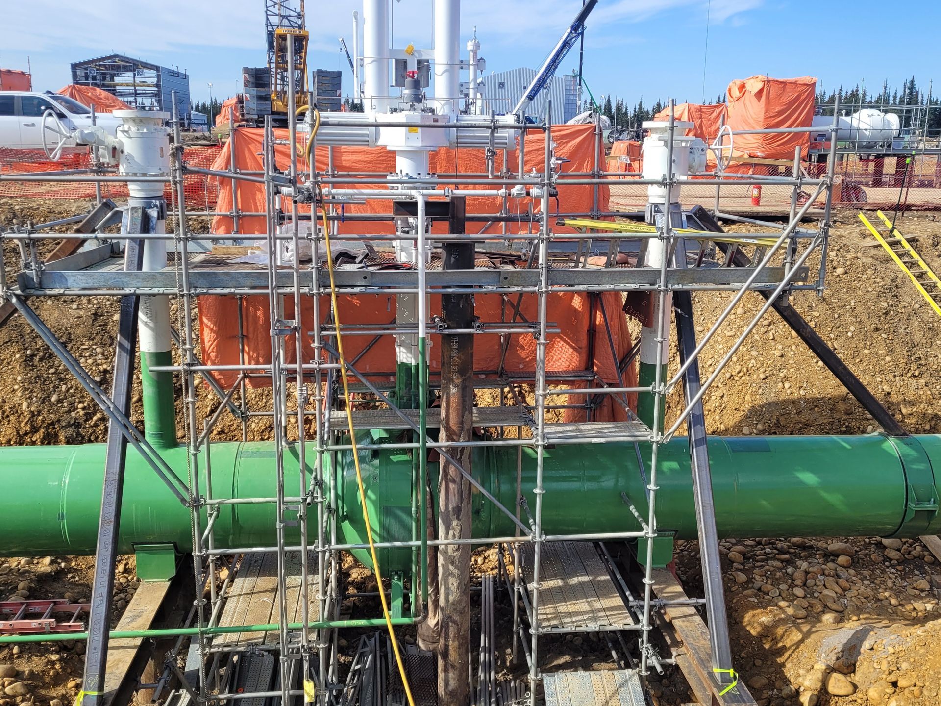 Active pipeline construction site with green pipe installation and scaffolding setup