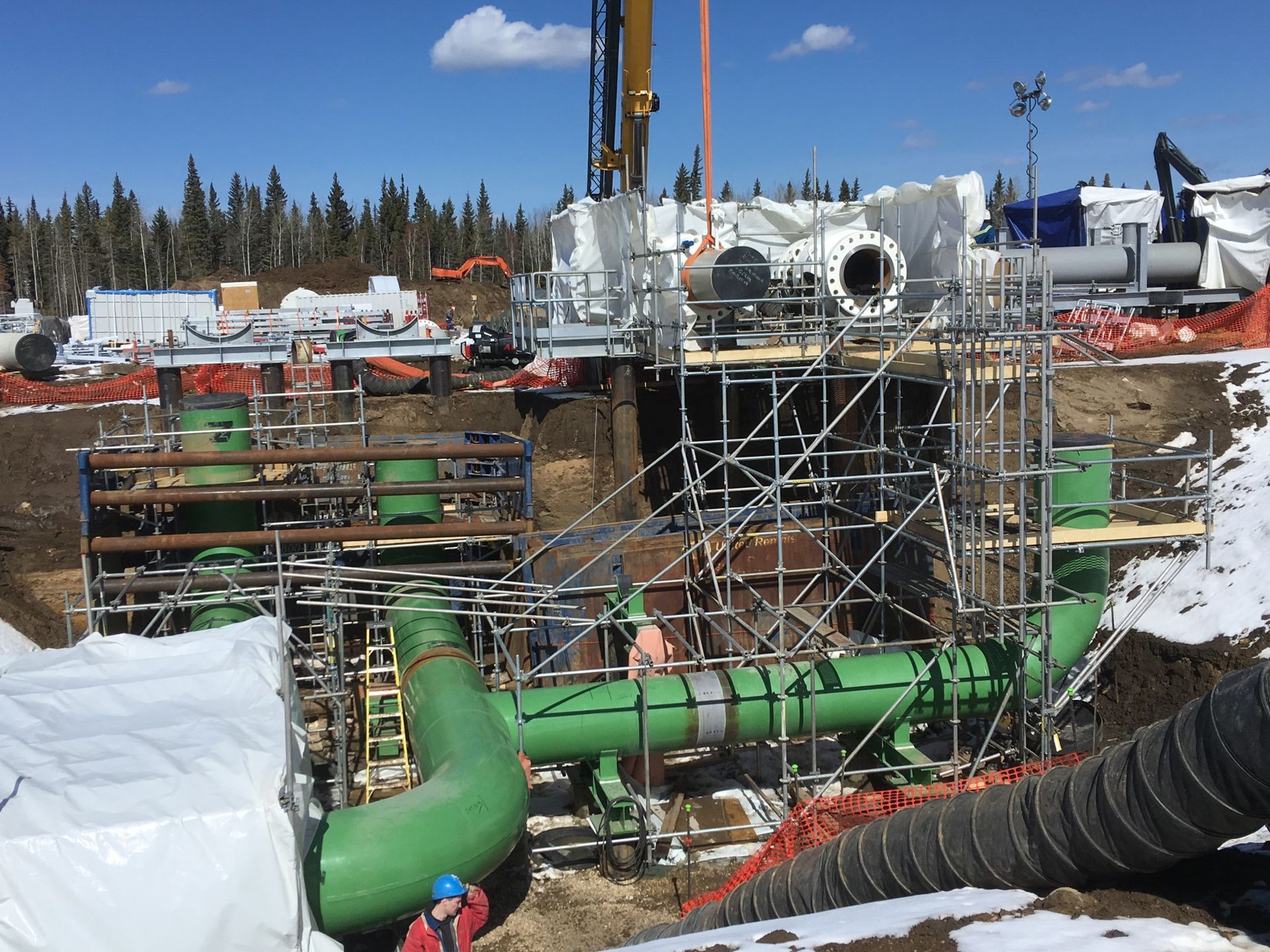 Industrial site with green coated pipes and scaffolding during pipeline coating operations