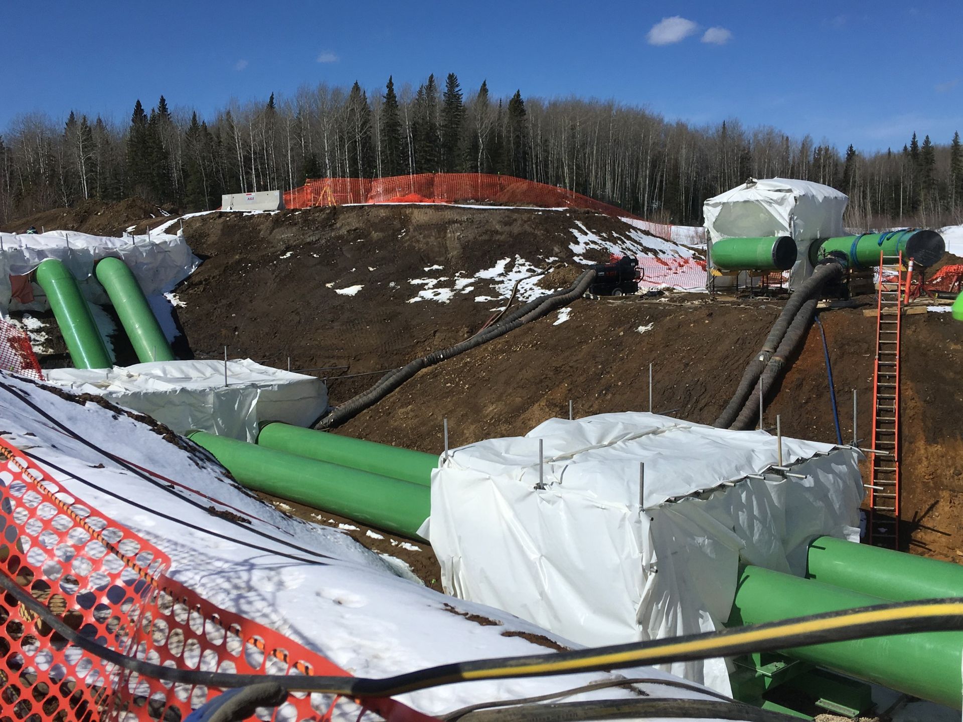 Pipeline project in a forested area with coated pipes and temporary insulation enclosures
