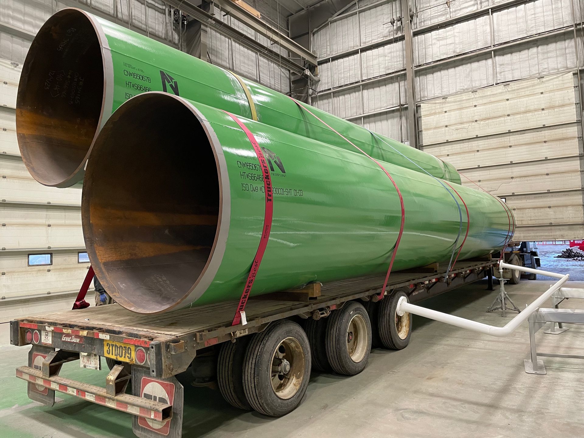 Multiple large-diameter pipes secured on a flatbed trailer after undergoing blast cleaning and coating