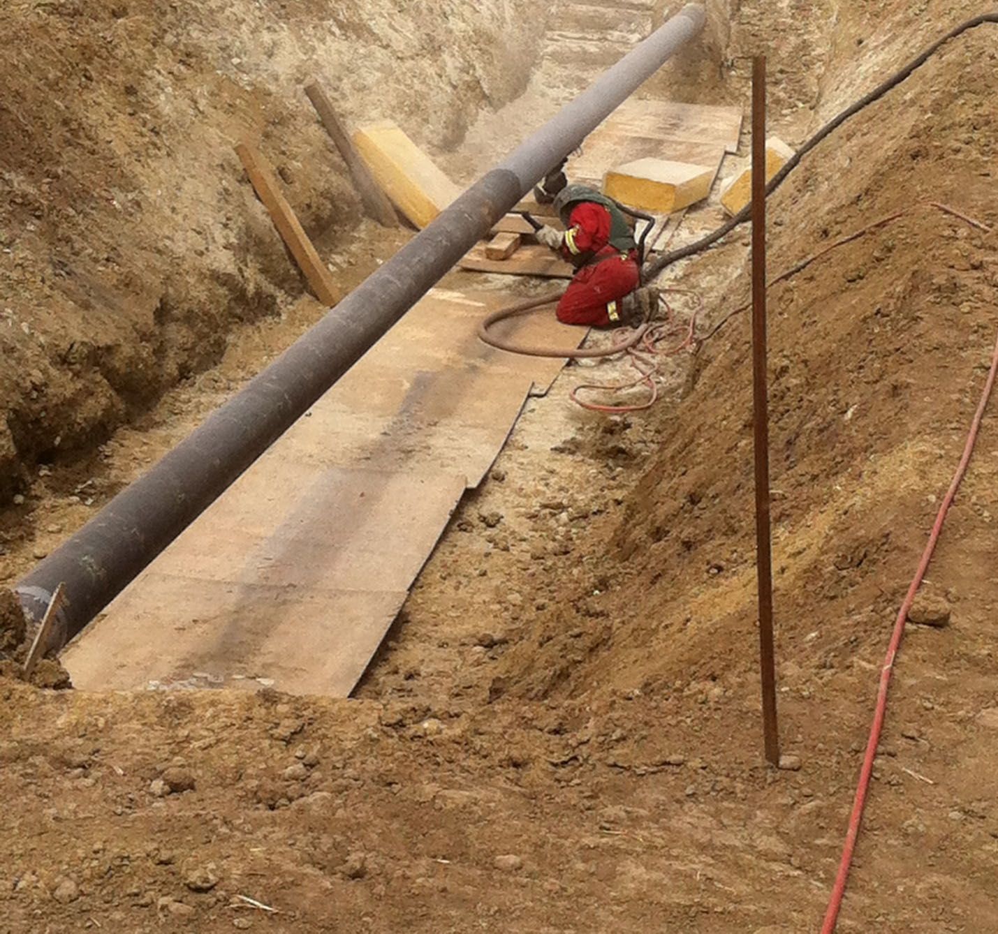Worker performing pipeline construction tasks in trench with exposed steel pipe