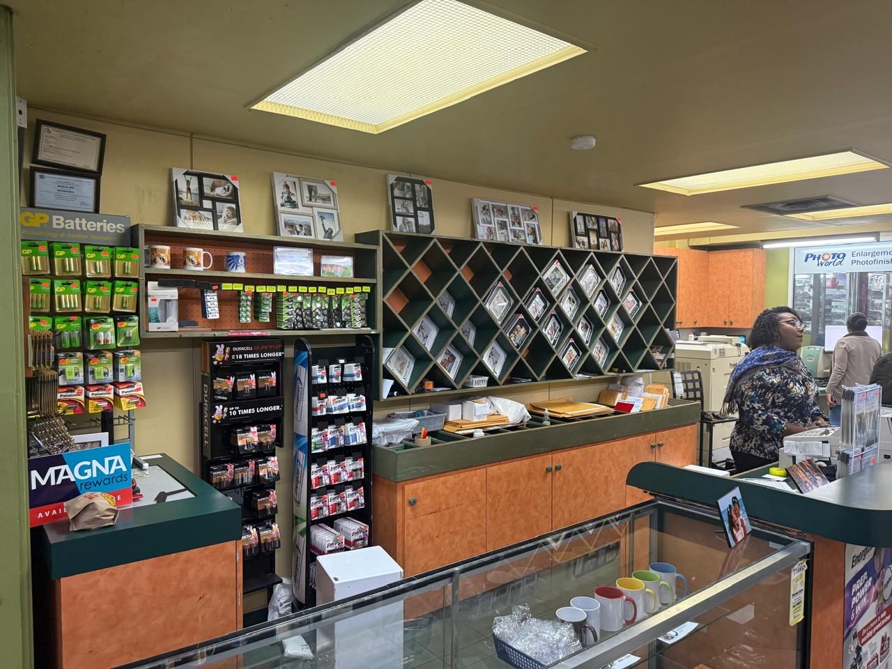 Interior of a store. Display shelves stocked with items, a customer at counter, and warm lighting.