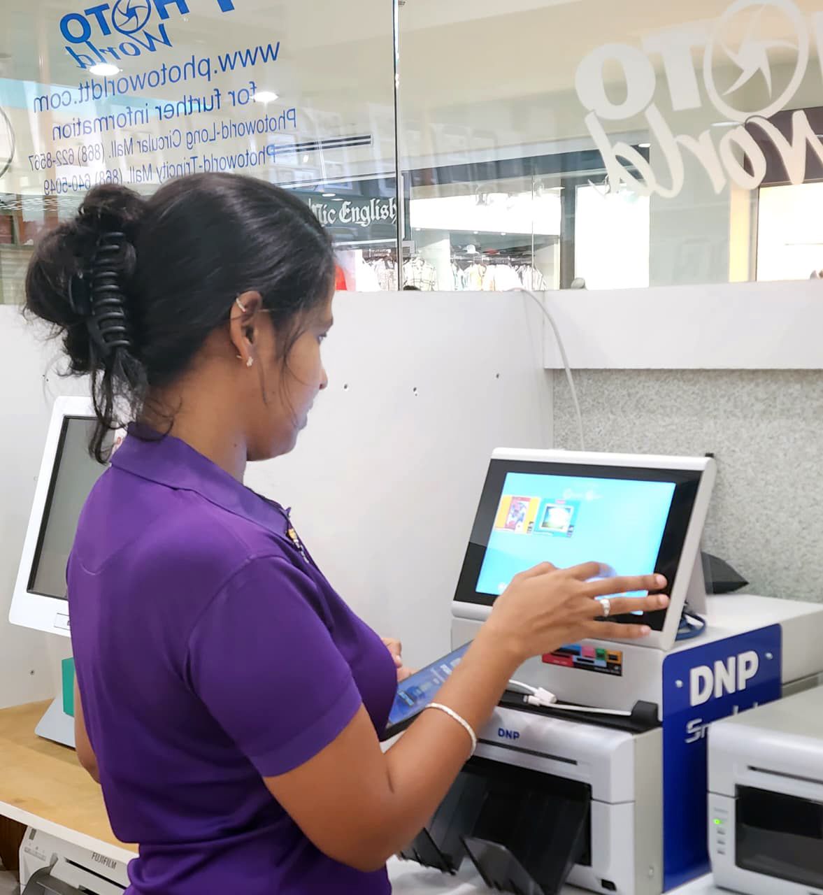 Woman in purple shirt using a touchscreen computer at a Photo World store.