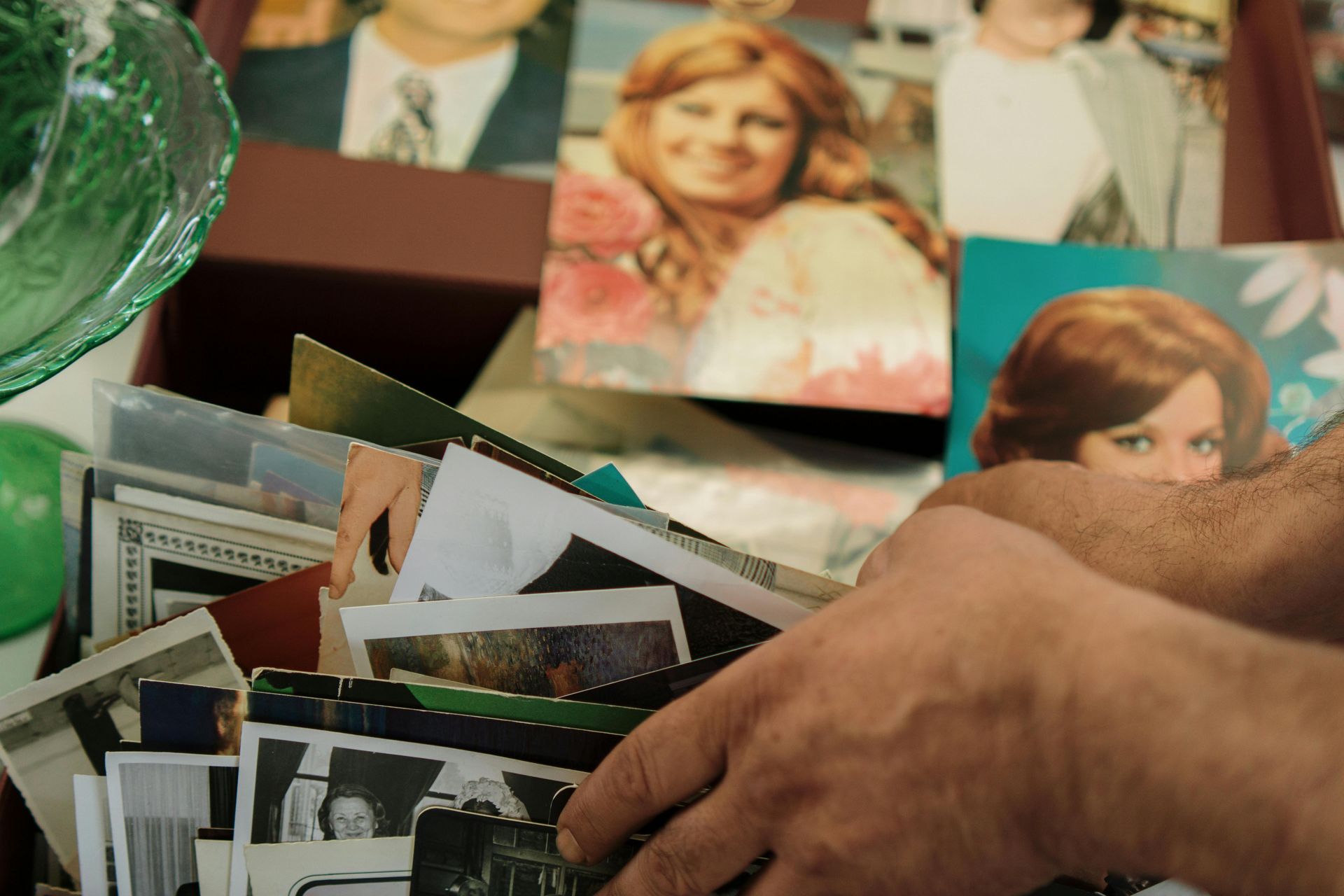 Hands sorting through a box of vintage photos, some featuring a woman with red hair.