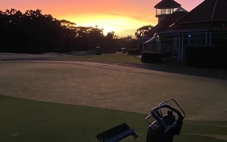 a person is standing on a golf course with a sunset in the background .