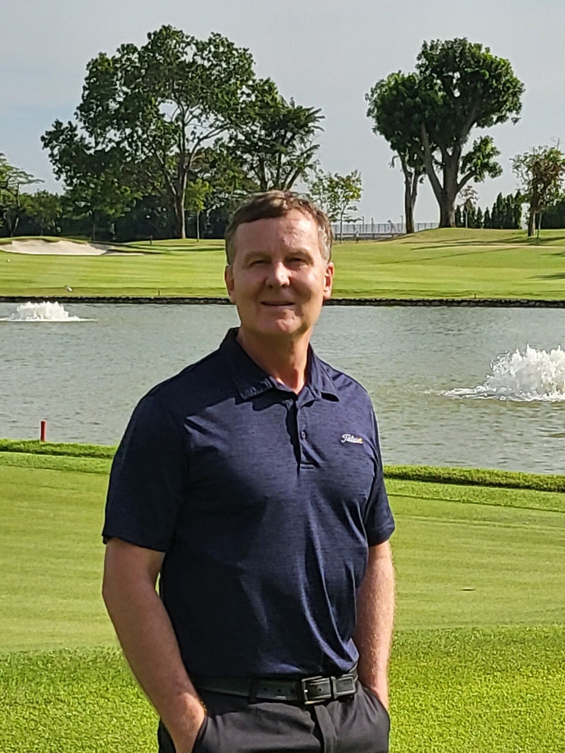 A man is standing on a golf course with his hands in his pockets.