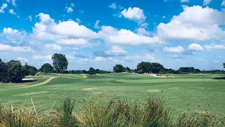 A golf course with a blue sky and white clouds in the background.
