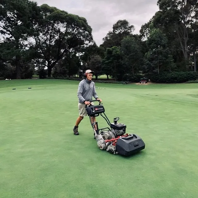 A man is pushing a lawn mower on a golf course