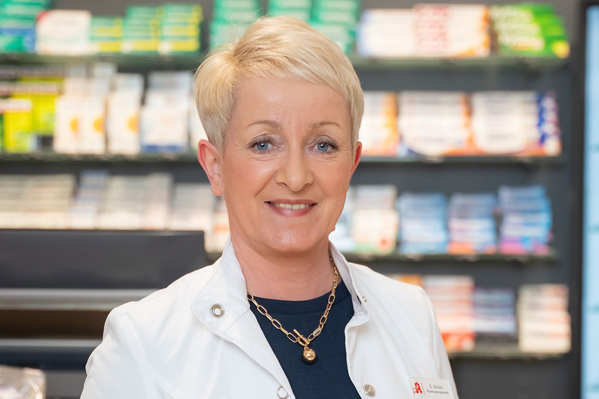 Eine Frau im weißen Kittel steht vor einer Apotheke.