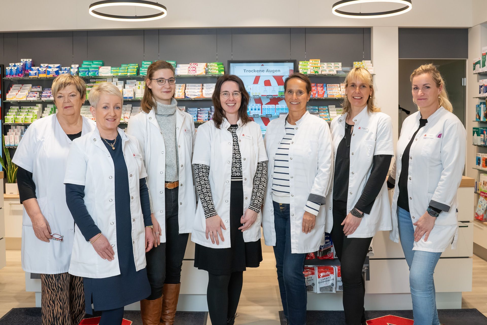 Eine Gruppe von Frauen in weißen Kitteln posiert in einer Apotheke für ein Foto.