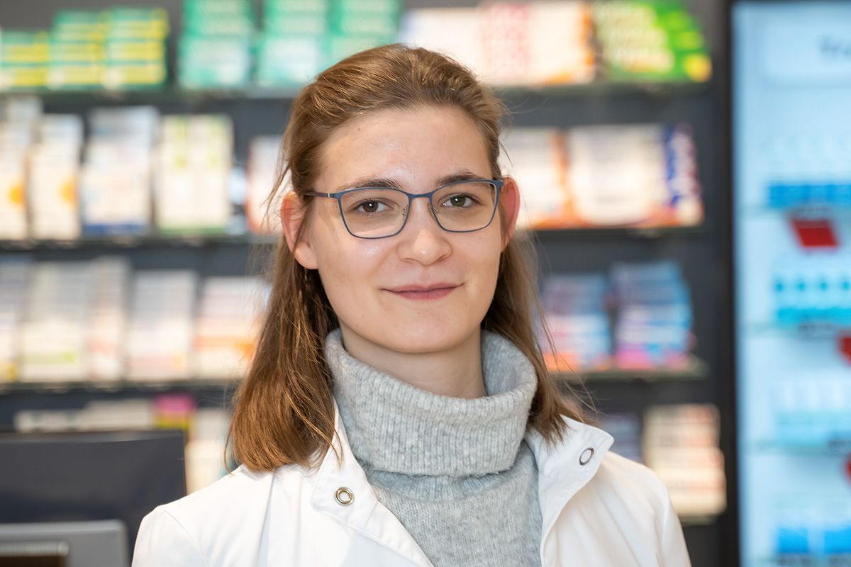 Eine Frau mit Brille und Pullover steht in einer Apotheke.