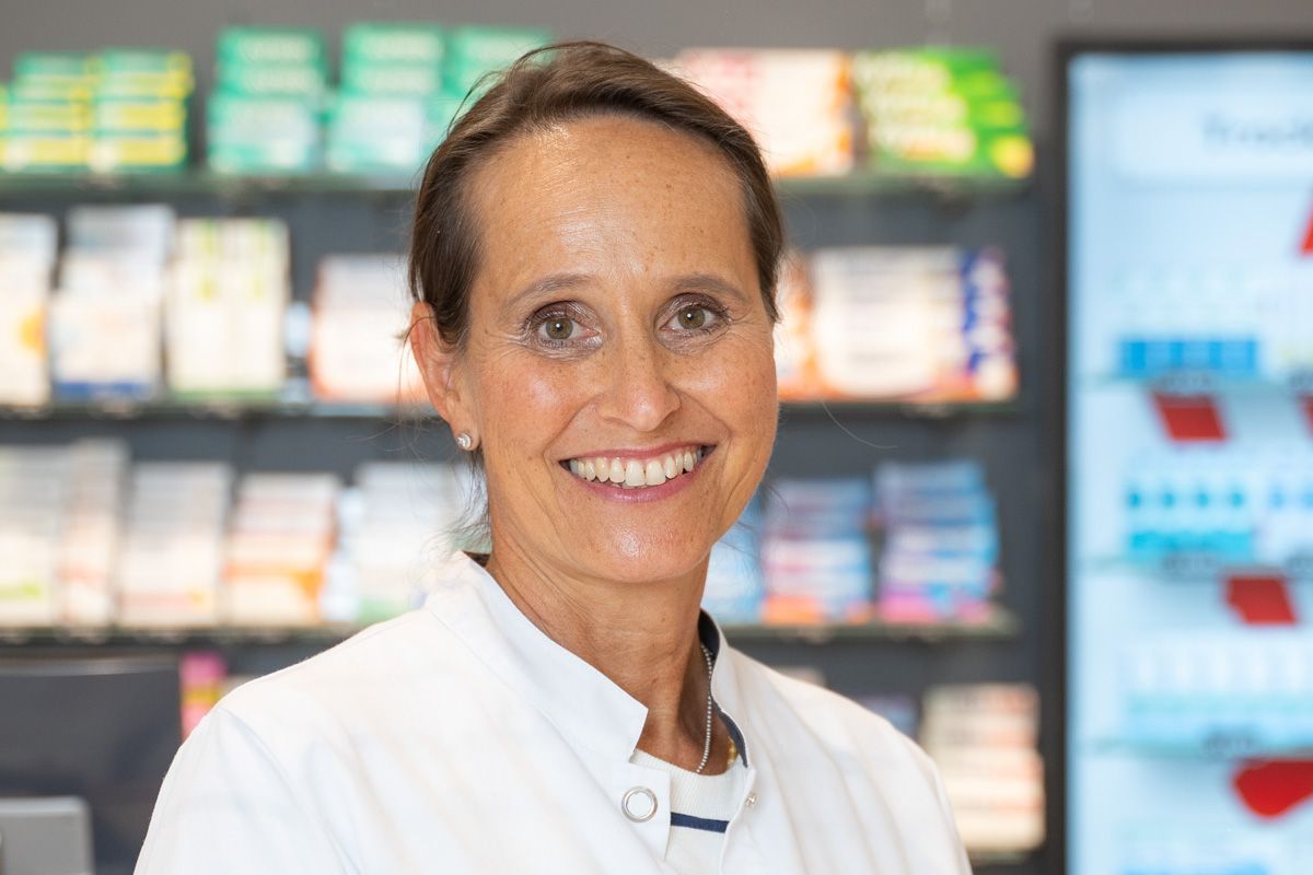 Eine Frau im weißen Kittel lächelt in einer Apotheke.