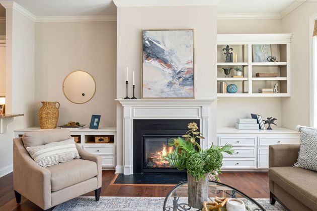 Cozy living room with beige chairs, a lit fireplace, and built-in shelves with decor and books.