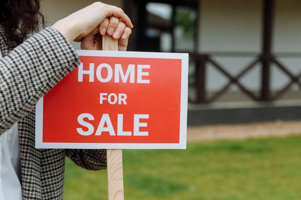Person holding a red and white “FOR SALE” sign