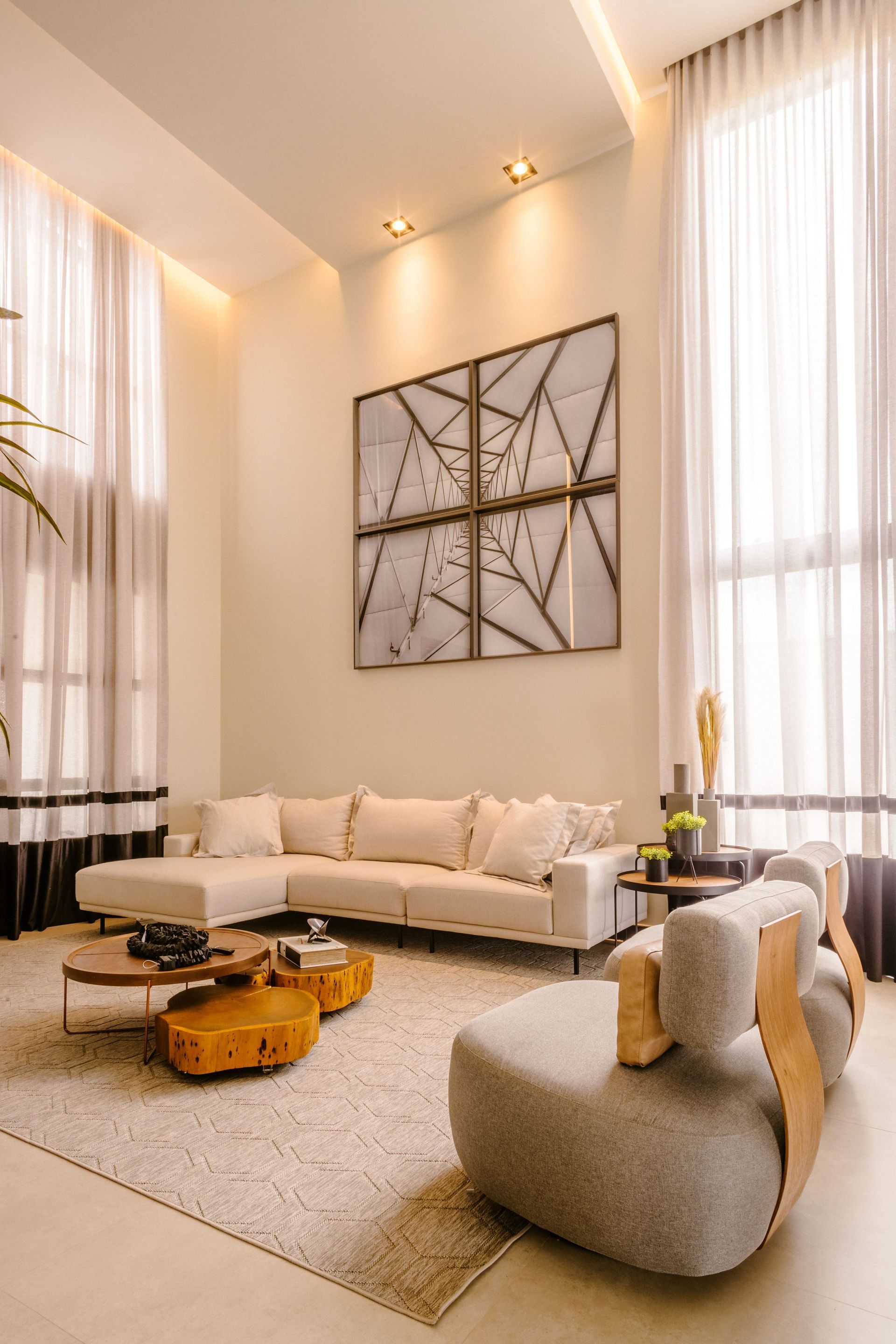 Modern living room with tall windows, beige sectional sofa, abstract wall art, and cozy neutral decor
