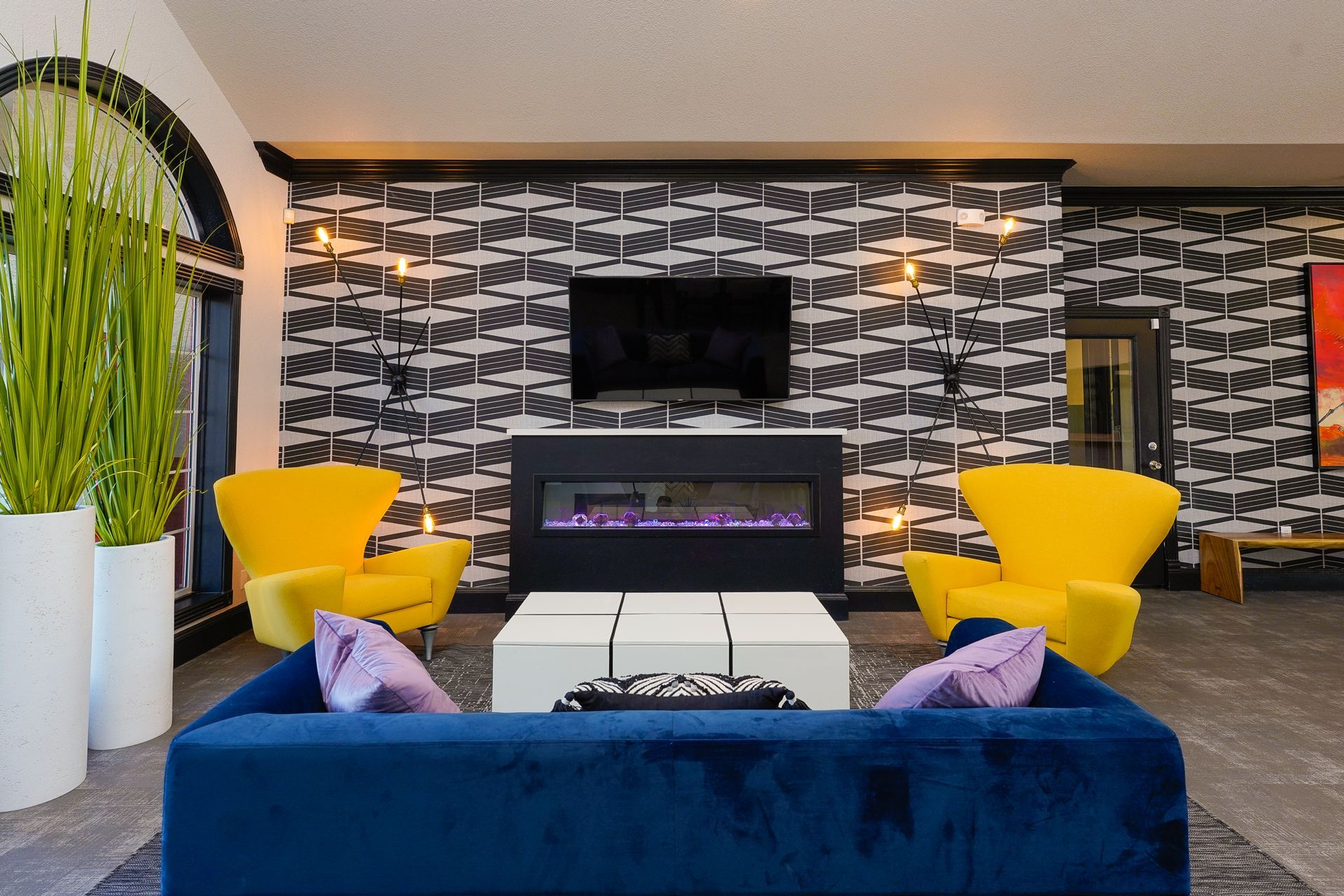 Living room: blue sofa, yellow chairs, fireplace, patterned wallpaper, TV, and decorative plants.